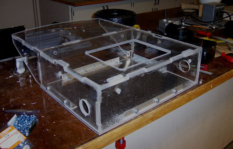 The transparent acrylic chassis of the cart on a workbench, its drilled panels and mounting frame visible.